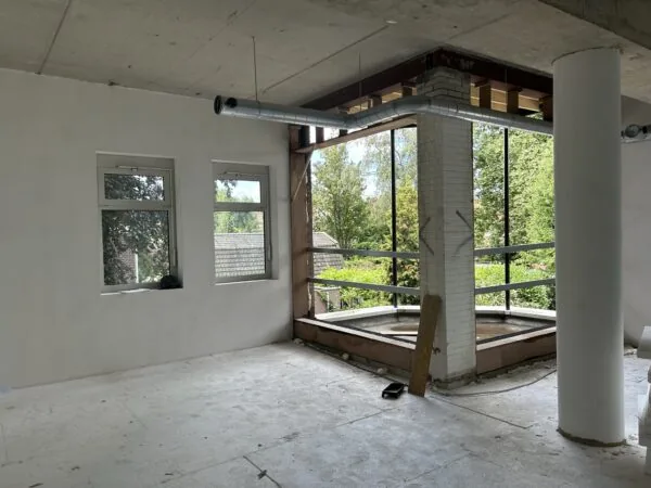 Interieur van een pand aan de Bergse Dorpsstraat in verbouwing met grote ramen en zicht op groen.